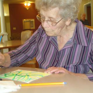 An elderly woman engaged in drawing during an art activity.