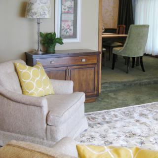 A cozy living room with an armchair adorned with yellow cushions, a wooden cabinet, and a floral carpet.