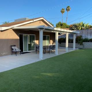 A modern house with a spacious backyard, featuring a patio and outdoor furniture under a clear blue sky.