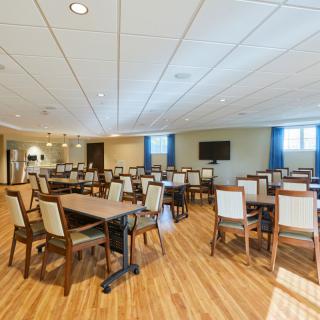 An empty dining room with neatly arranged tables and chairs, featuring wood flooring and ceiling lights.
