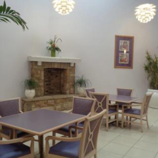 A cozy indoor seating area with tables and chairs near a fireplace, adorned with plants and soft lighting.