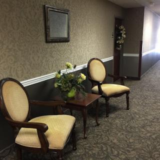 A cozy seating area in a hallway, featuring two elegant chairs and a small table adorned with flowers.