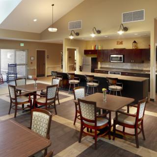 A modern dining and kitchen area with tables and chairs in a community space.