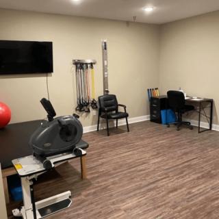 A well-equipped exercise room featuring a stationary bike, TV, and various workout tools for physical therapy.