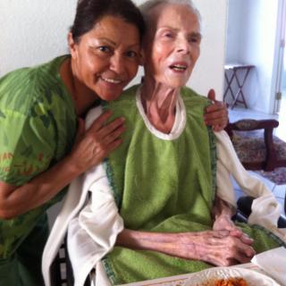 A caregiver smiles next to an elderly person during mealtime.