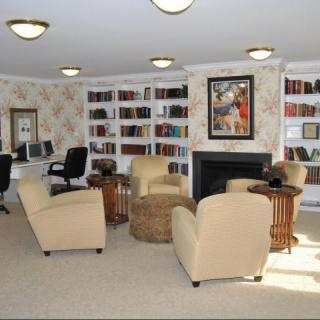 A cozy library room with bookshelves, comfortable chairs, computers, and a fireplace.