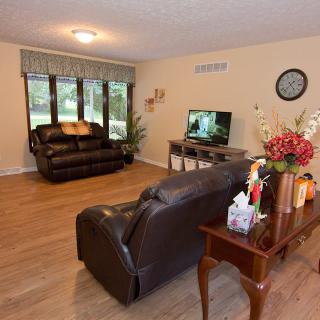 A cozy living room with leather sofas, a TV, and large windows providing natural light.