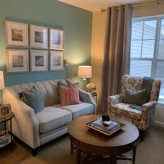 A cozy living room with a sofa, armchair, and coffee table, decorated with pillows and wall art.