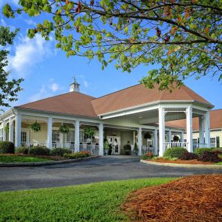 A large building with a red tiled roof and white pillars, surrounded by landscaped grounds and trees.