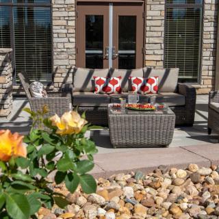 A cozy outdoor patio with wicker furniture, colorful cushions, and surrounding garden landscaping.