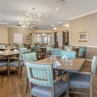 A well-lit dining room with neatly arranged tables and chairs, featuring elegant light fixtures.