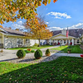 A charming house surrounded by a well-maintained yard, showcasing autumn colors under a bright blue sky.