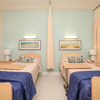 A well-lit hospital room featuring two patient beds with light blue walls and bedside lamps.