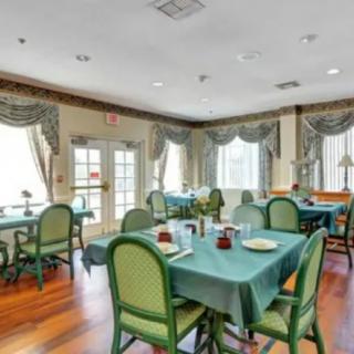 A cozy dining room with neatly arranged tables and chairs, featuring elegant curtains and a wooden floor.