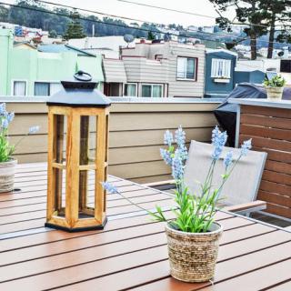 A rooftop deck with a wooden table featuring a lantern and potted plants, overlooking an urban neighborhood.