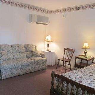 A cozy living space with a floral sofa, a wooden chair, two table lamps, and a patterned bedspread.