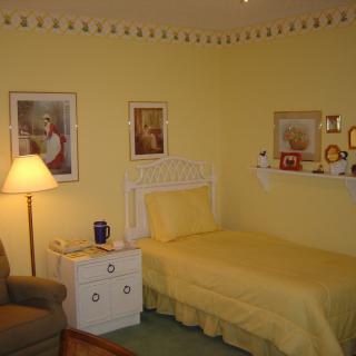 A cozy bedroom with yellow walls and a single bed, featuring framed artwork and a bedside lamp.