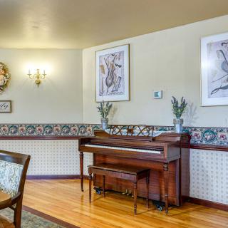 A cozy living room features a wooden piano against an artistically decorated wall, complete with framed artwork and elegant lighting.