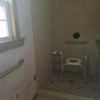 An accessible bathroom with a shower chair and grab bars.