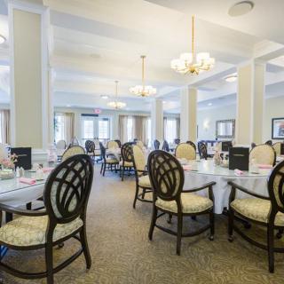 An elegant dining room with neatly arranged tables and chairs, illuminated by chandeliers.