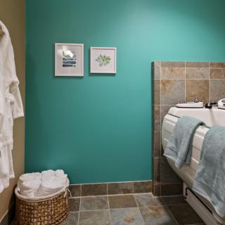 A well-decorated bathroom featuring a turquoise wall, framed artwork, and neatly arranged towels beside a tiled bathtub.
