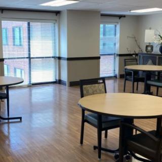 An empty room with round tables and chairs, featuring large windows.