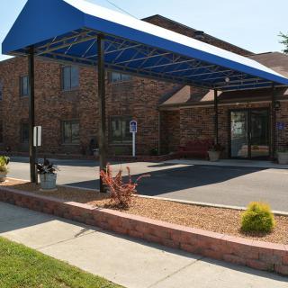 A building entrance with a blue awning and adjacent parking area.