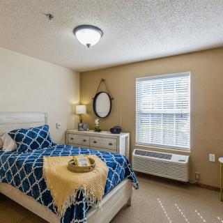 A cozy bedroom with a neatly made bed, a dresser with a mirror, and a lamp near the window.