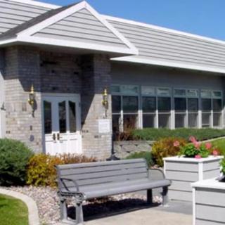 A modern building with large windows, surrounded by landscaping and a bench in the foreground.