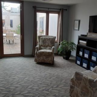 A cozy living room with armchairs, a TV stand, and large windows allowing natural light.
