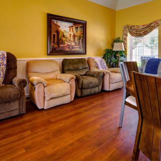 A cozy living room with a row of recliners, hardwood floors, and a dining area.