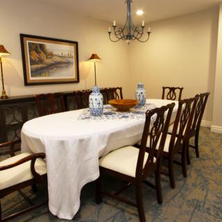 A well-furnished dining room featuring a table with a white tablecloth, surrounded by wooden chairs and adorned with decorative vases.