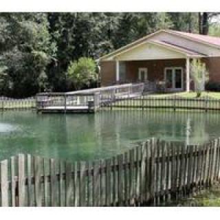 A tranquil pond surrounded by a wooden fence with a house and deck in the background.