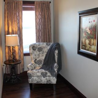 A cozy reading nook featuring a floral armchair, soft throw blanket, and warm lighting.