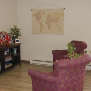 A cozy office seating area with two chairs, a world map on the wall, and a shelf with books and plants.