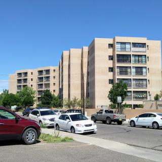 A street view featuring modern apartment buildings alongside parked cars under a clear blue sky.