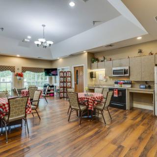 A spacious and modern dining area with a kitchen, featuring wood flooring and elegant lighting.