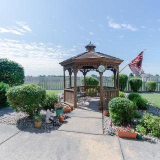 A wooden gazebo surrounded by a landscaped garden with decorative plants and an American flag in the background.