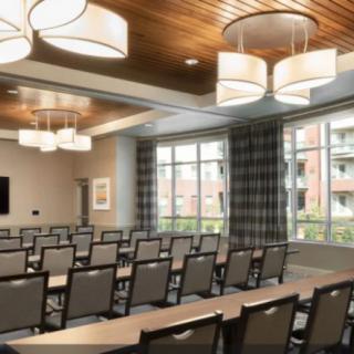 A modern conference room with rows of tables and chairs, featuring large windows and stylish lighting.