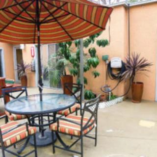 A cozy outdoor patio with a table and chairs under an umbrella, surrounded by plants.