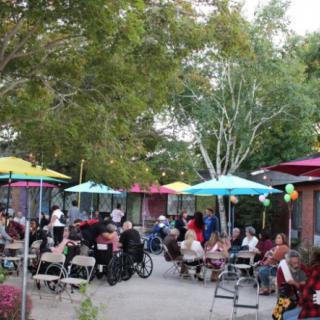 A lively outdoor gathering with people seated under colorful umbrellas.
