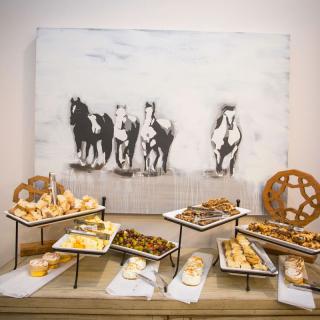 A stylish buffet setup featuring an array of hors d'oeuvres and cheese platters, with a backdrop of horse-themed artwork.