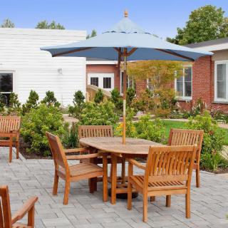 An inviting outdoor patio with wooden furniture and a large umbrella, surrounded by lush greenery.