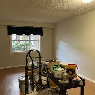 A partially renovated room featuring a window, tools, and paint supplies.