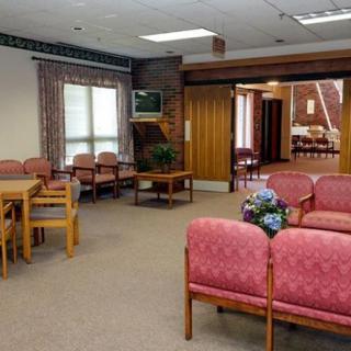 A spacious waiting room with pink upholstered chairs, a small table, and a television mounted on the wall.