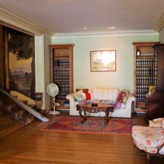 A cozy living room with a sofa, chairs, bookshelves, and a large painting on the wall.