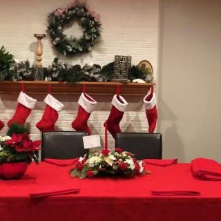 A festive Christmas setup with stockings hanging over a mantel and a table adorned with a red tablecloth and floral centerpiece.