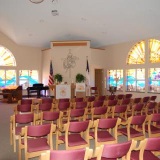A serene interior view of a chapel with rows of chairs and colorful stained glass windows.