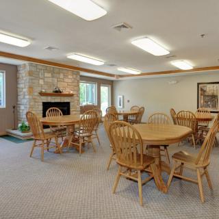 A cozy dining area with wooden tables and chairs, featuring a stone fireplace and large windows.