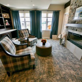 A cozy living room featuring plaid chairs, a modern fireplace, and large windows with curtains.